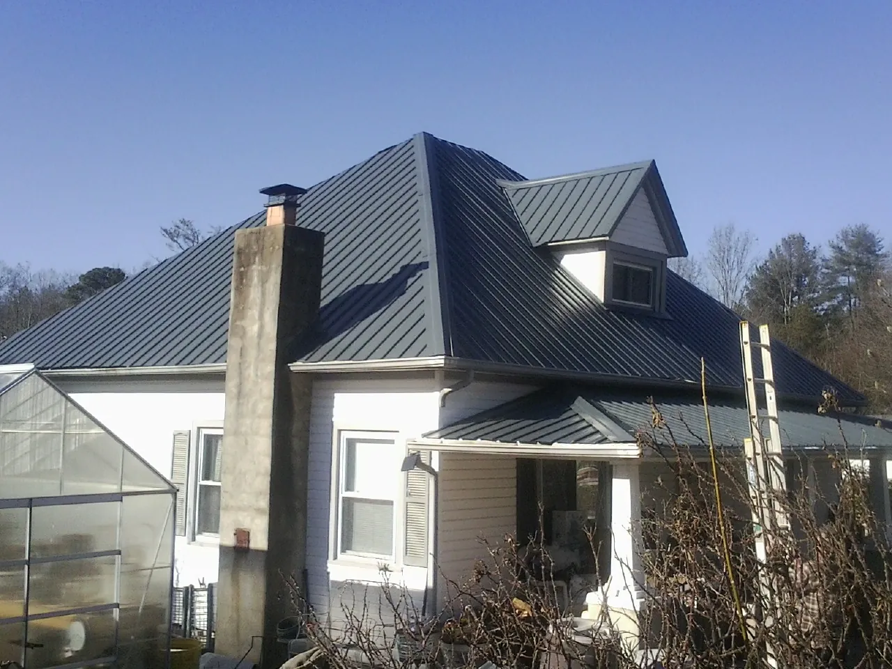 Dark blue standing seam metal roof on a white farmhouse with dormer — Slate & Tile Roof Repair by Roofing Brothers in Seneca