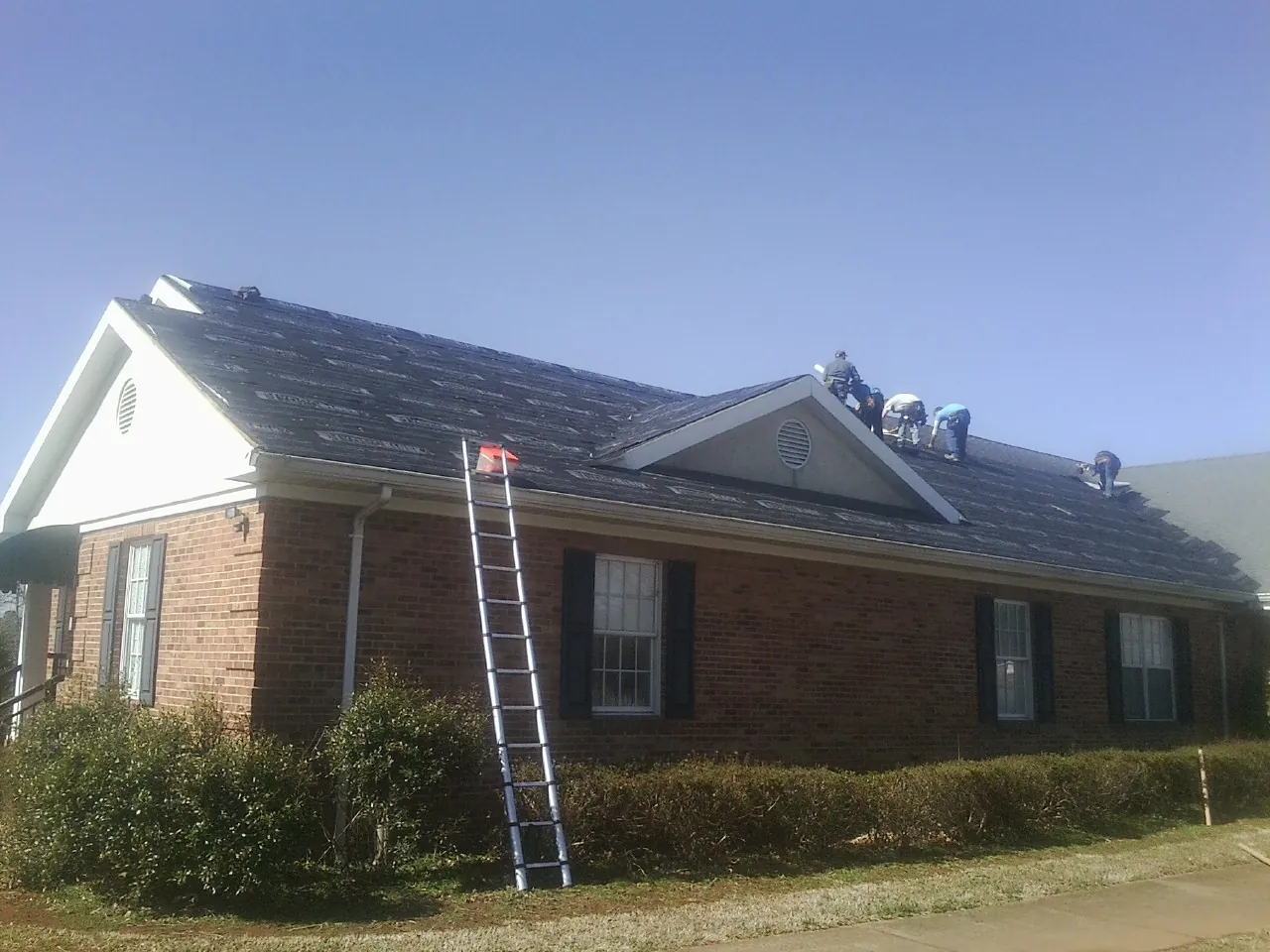 Crew tearing shingles off a brick ranch roof with a ladder set — Metal Roof Repair work by our crew in Seneca
